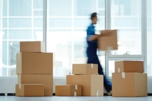 Verwischte Bewegungsaufnahme eines modernen Büroangestellten, der mit einem vollgepackten Karton zu seinem neuen Büro geht und diesen dabei an einen Kunden übergibt